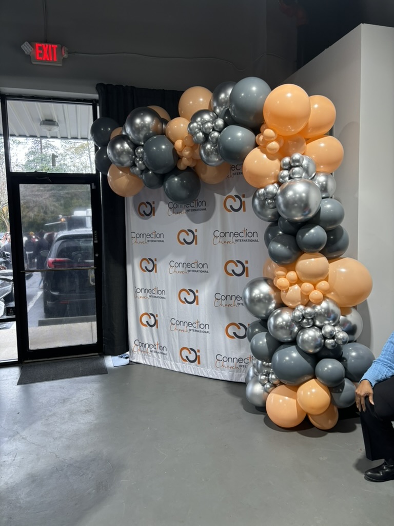 Step-and-repeat logo backdrop framed by a balloon garland in the client's brand colors, installed by Sharp Designs