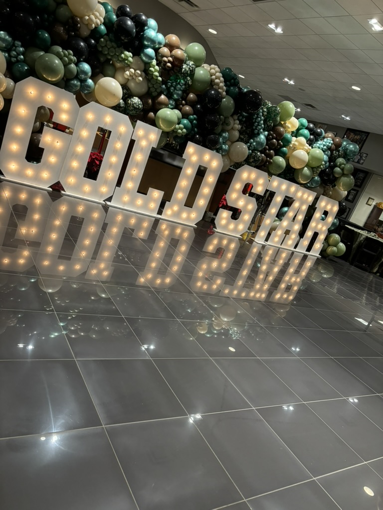 Lit marquee letters in front of a balloon wall on a light-up dance floor, styled by Sharp Designs