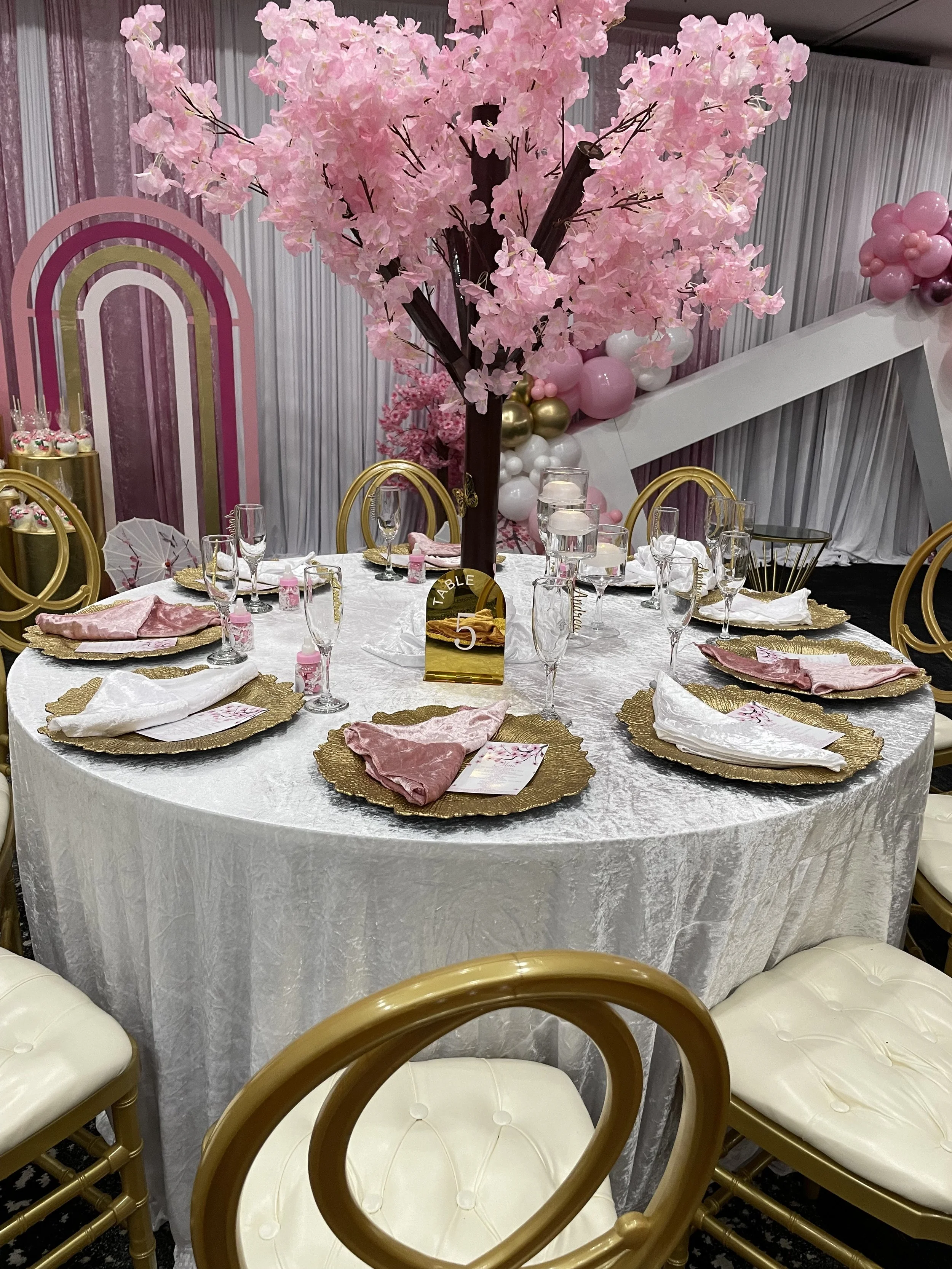 Pink baby shower tablescape with blossom trees and gold chairs