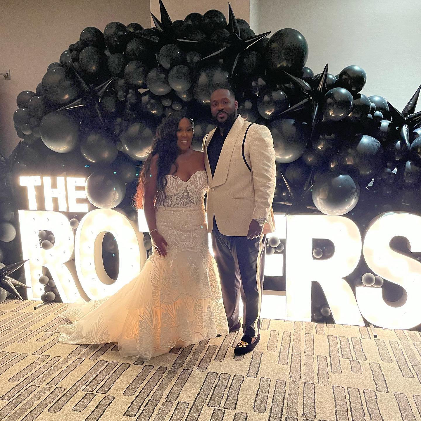 Couple in front of a black balloon wall and lit marquee letters